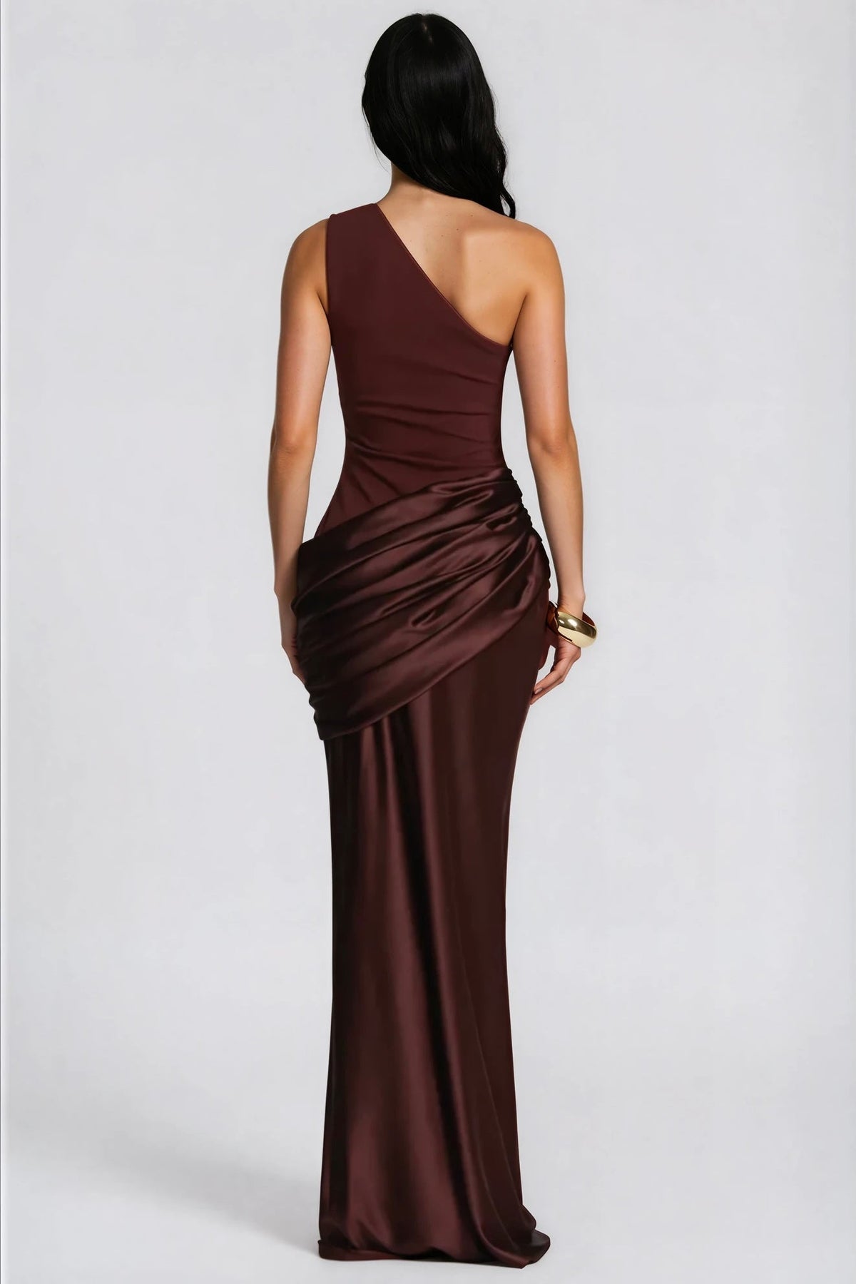 Back view of the brown dress, showing the asymmetric back, satin drape at the hip and a gold cuff on the wrist. 7