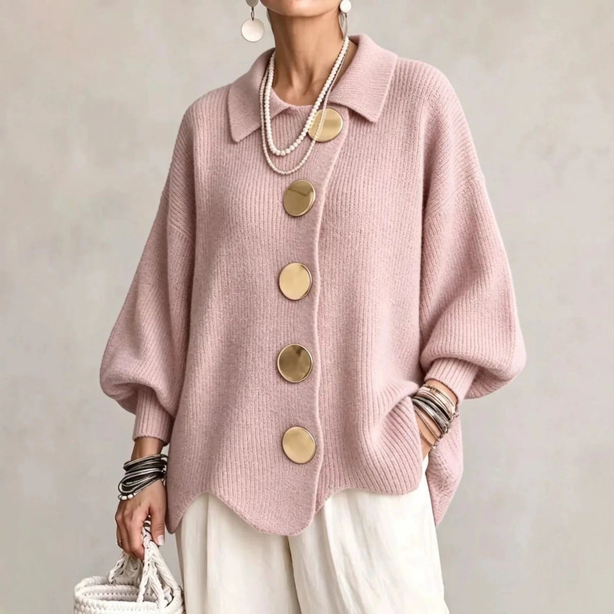 Soft pink ribbed cardigan on a model, with big gold buttons and balloon sleeves, worn with white trousers. 6