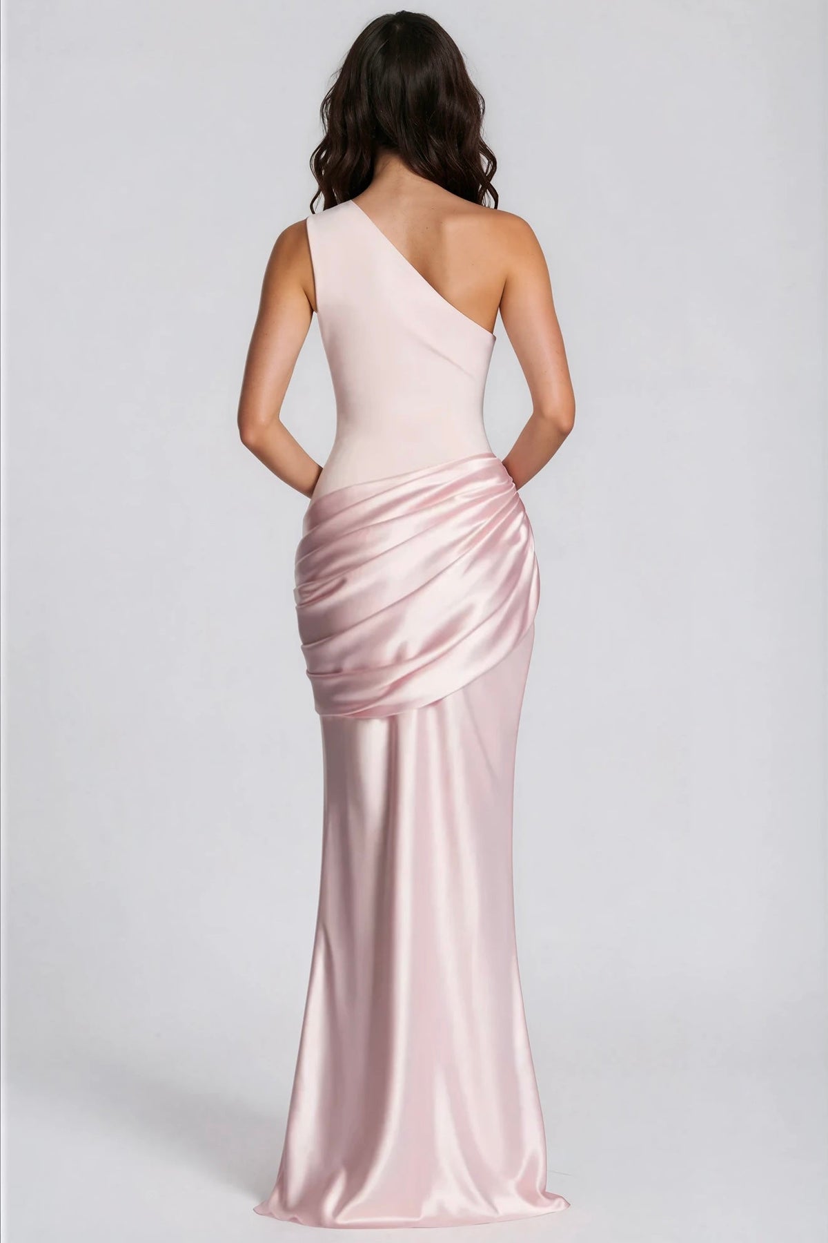 Back view of the pale pink one-shoulder maxi dress, showing the diagonal neckline, fitted bodice and draped satin hip detail. 31