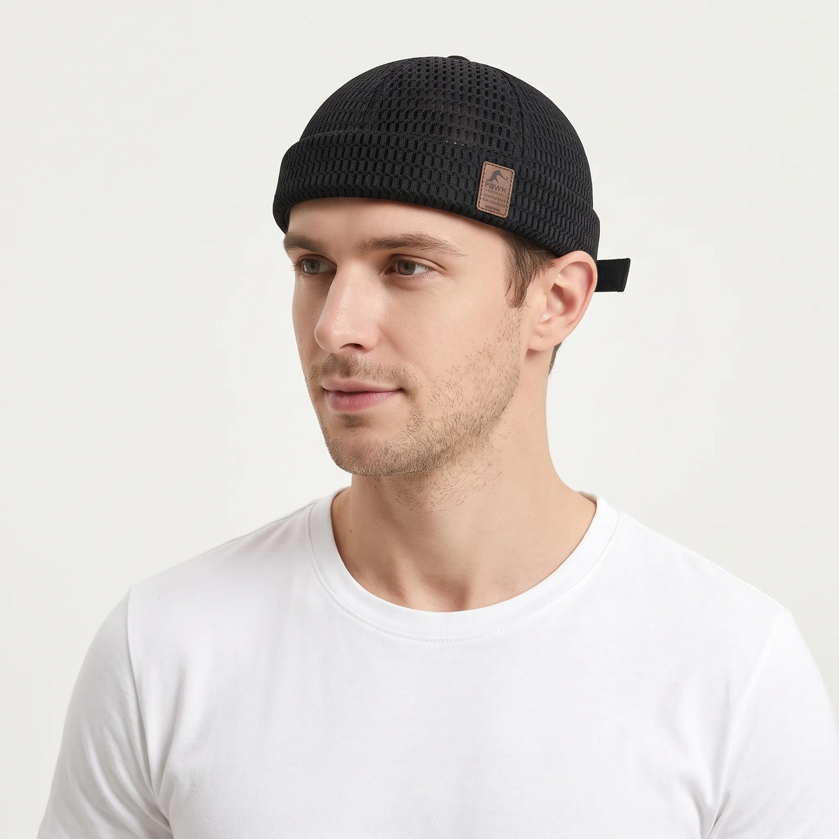 Man in a white t-shirt wearing the black open weave brimless cap with a small leather patch 24