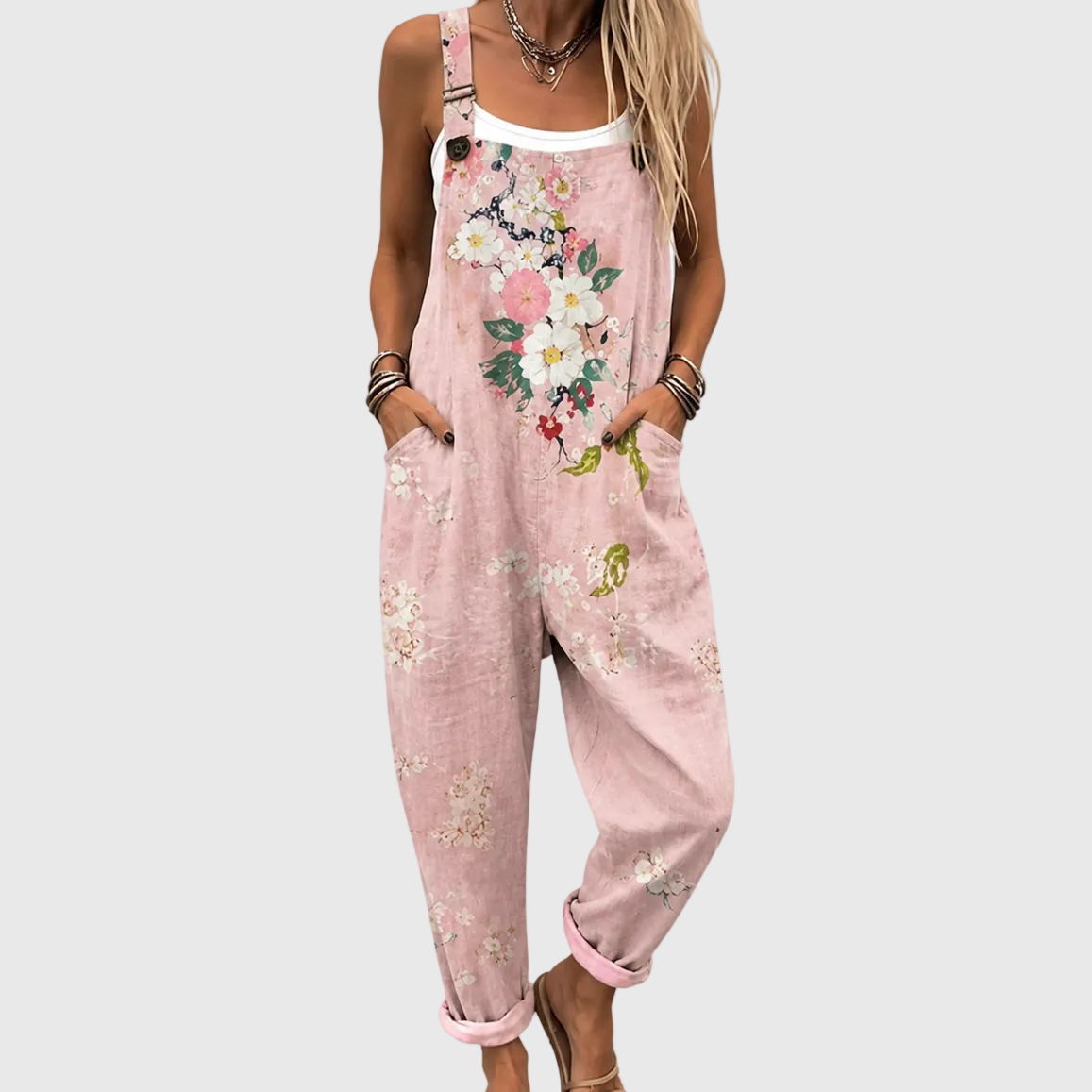 Close crop of the floral overalls worn over a white vest, hands in the side pockets, showing the strap buckle and flower print. 1