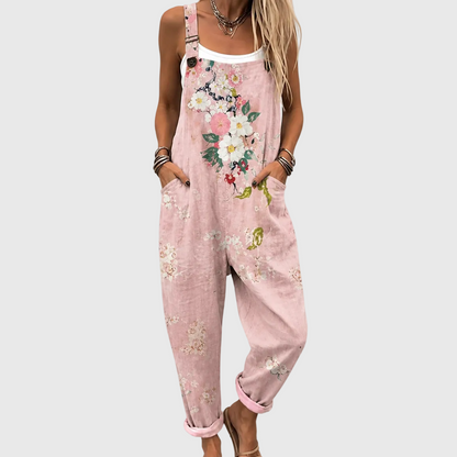 Close crop of the floral overalls worn over a white vest, hands in the side pockets, showing the strap buckle and flower print. 1