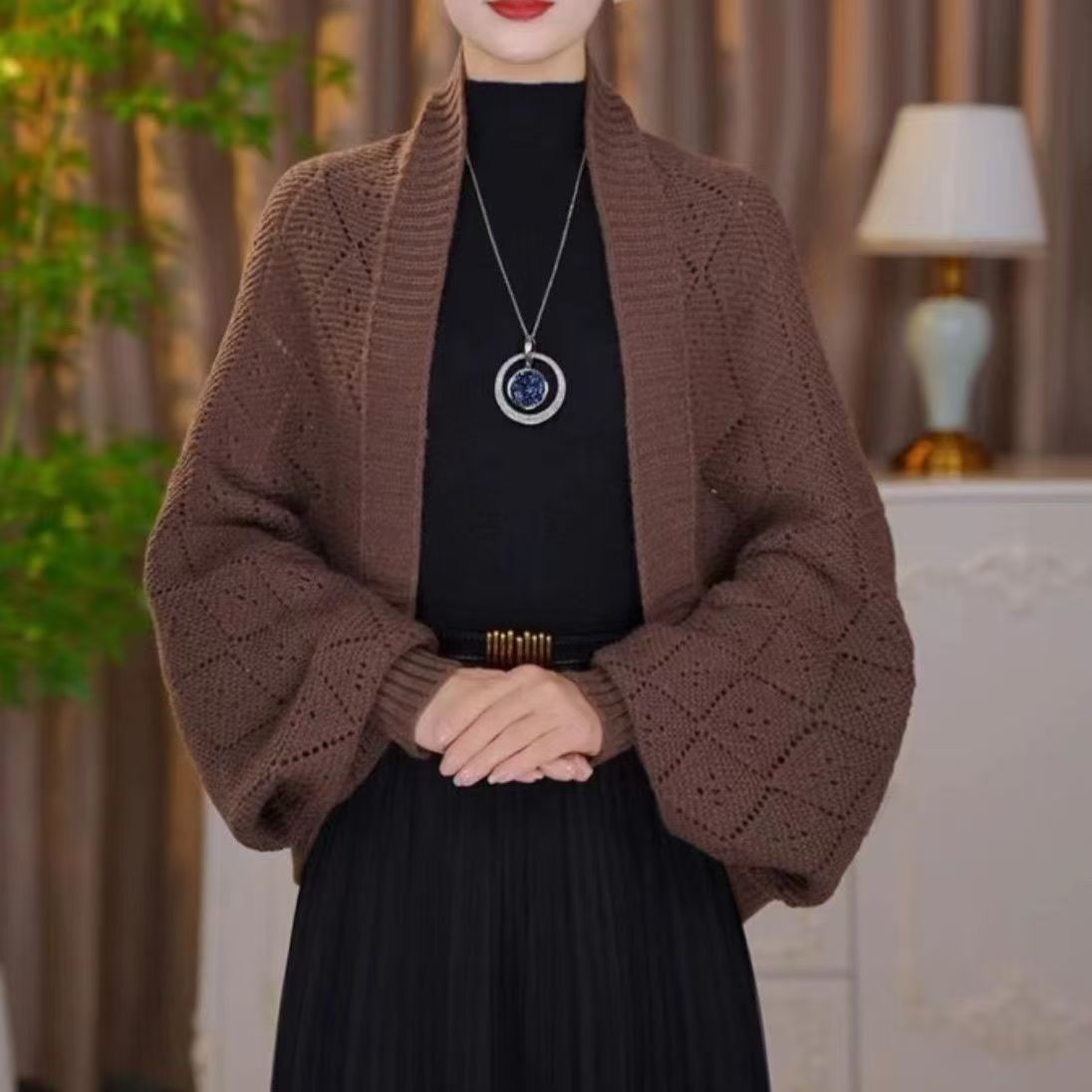 Model wearing the open knit shawl cardigan in chocolate brown with a pendant necklace and pleated skirt 2