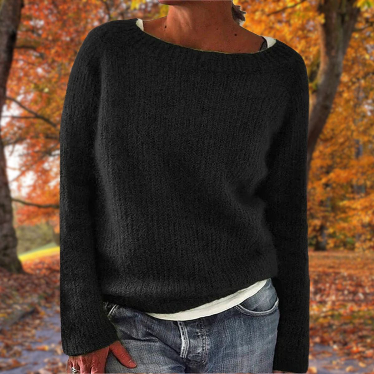 Model in the black version of the knit jumper, worn over a white top and jeans in an autumn park. 2