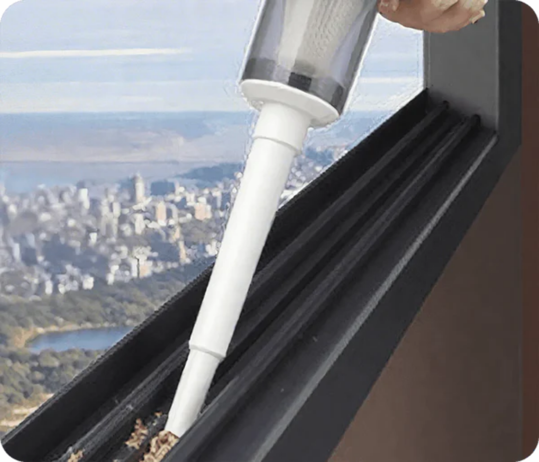 Narrow crevice tool attached to the handheld unit, sucking debris out of a window track with a hazy city view behind. 4