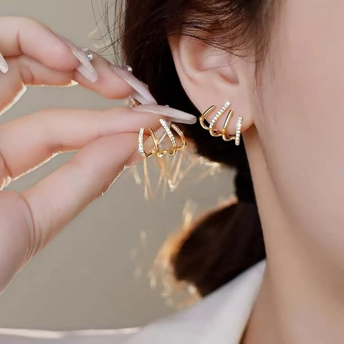 Close-up of the gold claw earring worn in an ear, with the matching one held between manicured fingers 2