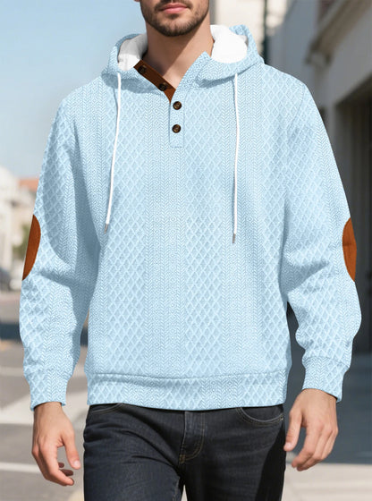Light blue diamond-textured hoodie worn by a model walking outdoors, front view with tan elbow patches 29