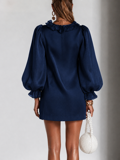 Back view of the navy dress on a model, showing the ruffled neckline, zip fastening, puff sleeves with ruffled cuffs and a straight short hem. 7