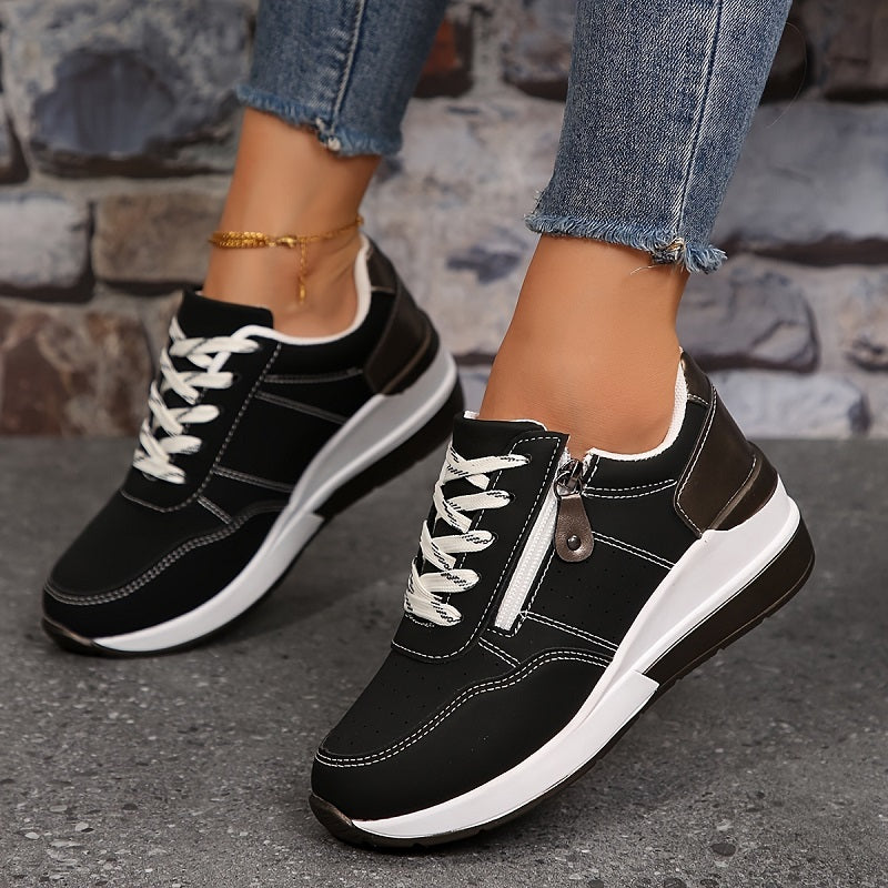 Black trainers with white laces, side zip and wedge sole, worn mid-step on a grey pavement 4