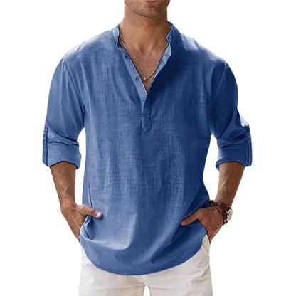 Man wearing the Henley shirt in blue, with a short button placket, rolled sleeves and hands in white trouser pockets. 2