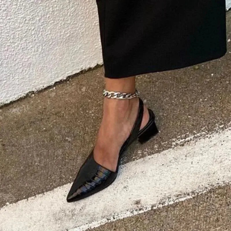 Close-up of a black croc-effect slingback on a foot, worn with a silver ankle chain 2