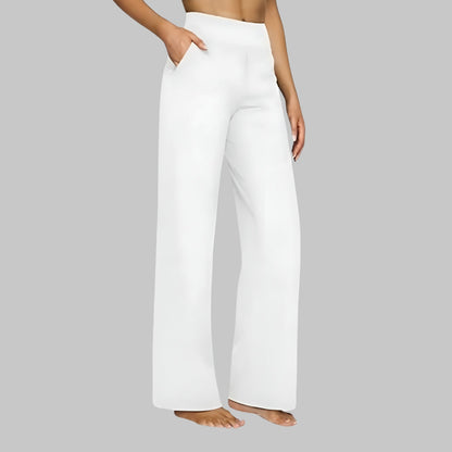 White version of the high-waist wide-leg trousers, side view, worn barefoot with a hand in the pocket. 8