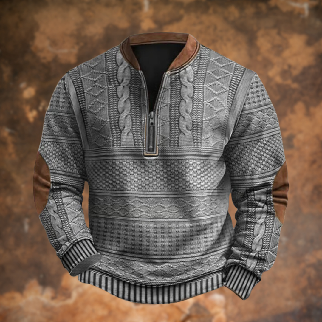 Front view of the grey version with cable and diamond knit panels, brown collar edging, half zip and tan elbow patches, on a rusty backdrop. 5