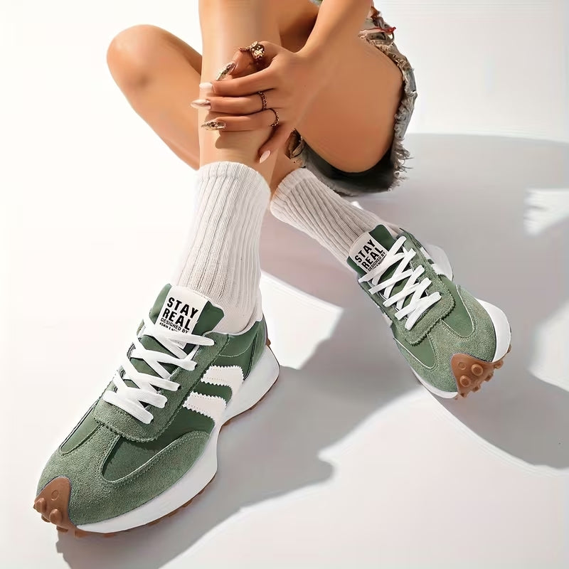 Model sitting with legs crossed, wearing green suede trainers with white stripes and ribbed white socks 7