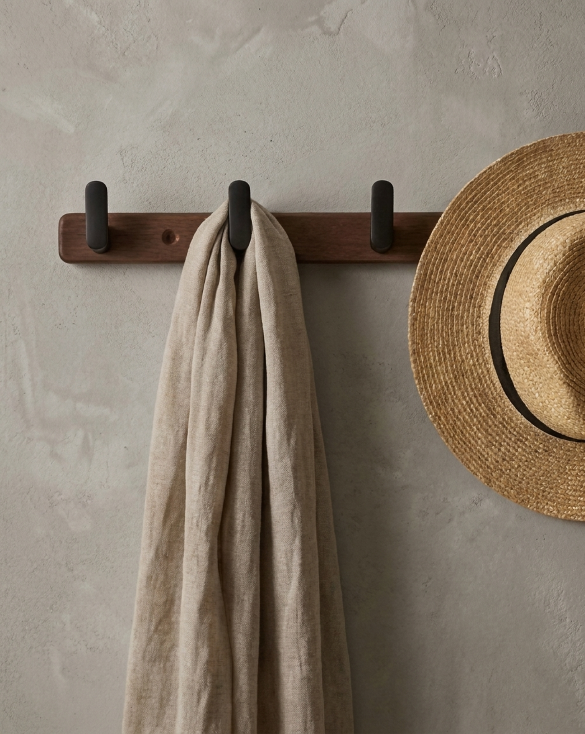 Close view of the rack on a grey wall holding a linen scarf and a straw hat 2
