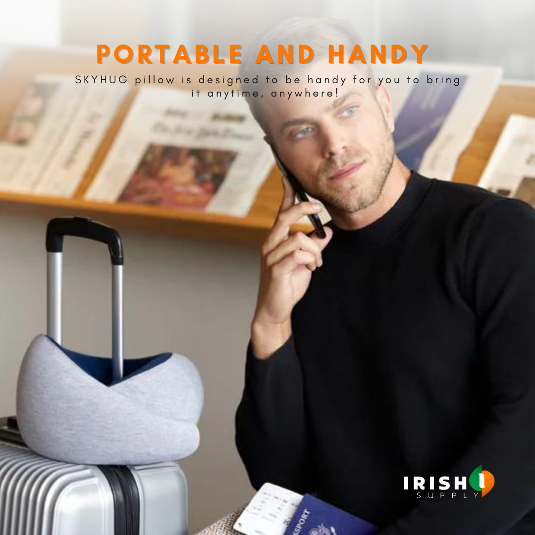 Man on a phone call in a waiting area, a grey neck pillow slotted over the handle of a suitcase beside him. 2