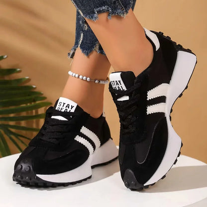 Black trainers with white stripes and chunky white platform sole, worn by a model against a beige backdrop 2