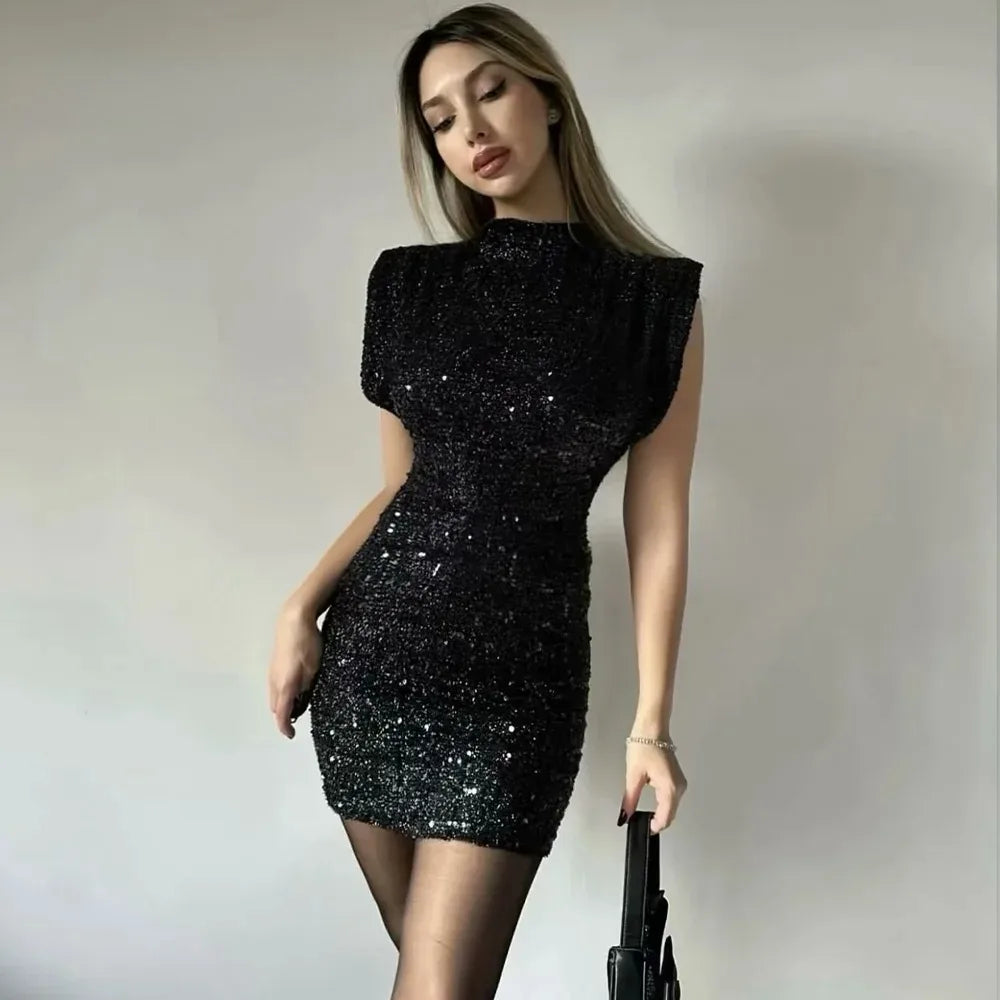Model in the black sequinned mini dress with sheer tights, holding a small black bag 2