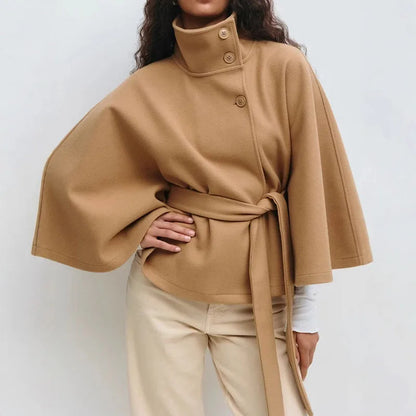Camel cape jacket worn with a hand on the hip, buttoned high collar, belt tied at the side 2