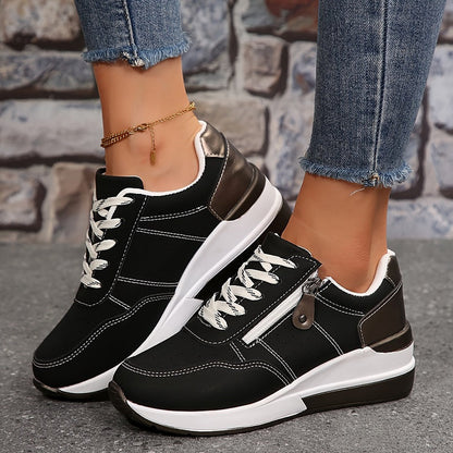 Black lace-up trainers with white stitching and side zip, worn with a gold anklet against brick 2