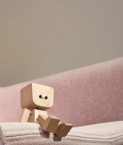 Small wooden figure with a smiling face sitting on the edge of a pink fabric sofa. 4