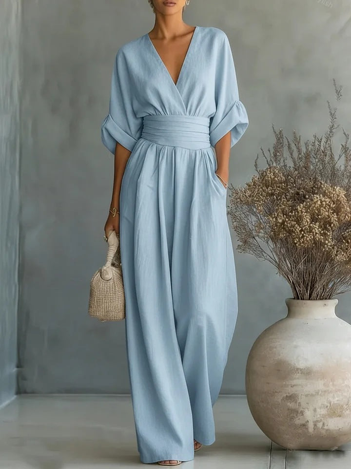 The jumpsuit in pale blue, worn by a model holding a woven bag next to a vase of dried flowers. 2