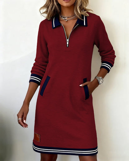 Burgundy dress with half zip and navy pocket trims, model standing with one hand in a pocket. 14