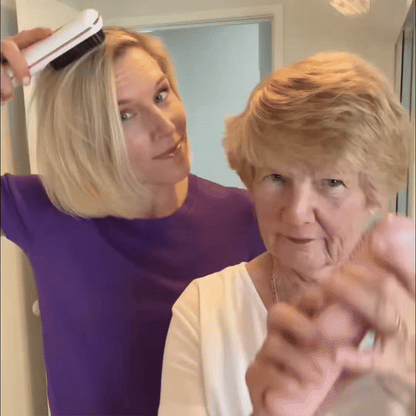 Blonde woman in a purple top using a white brush on her hair while an older woman with short hair stands in front. 9