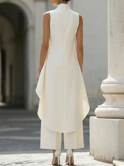 Back view in cream on a model, showing the centre back seam, high neck and rounded longer hem over the trousers. 13