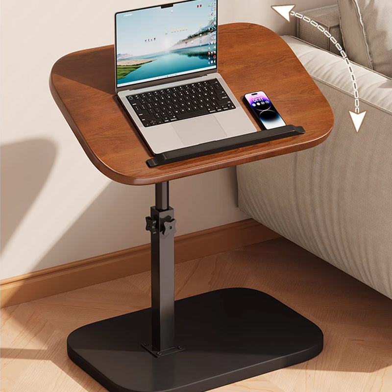 Dark wood-effect desk tilted beside a sofa with a curved arrow showing the top's movement, laptop and phone resting on it. 2