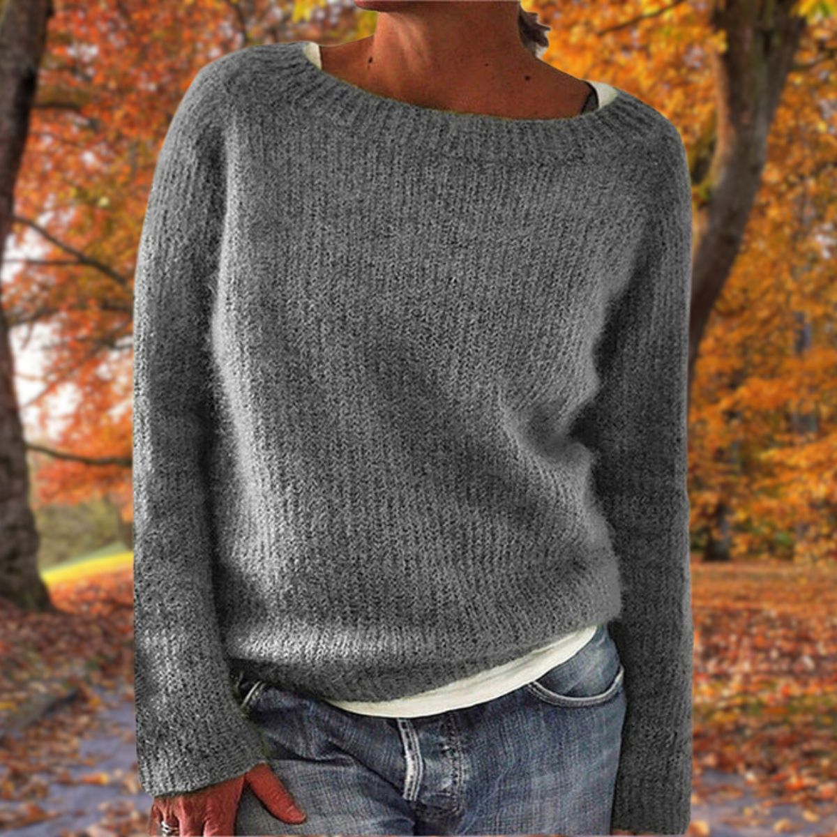 Model in the grey version of the textured knit jumper, worn over a white top and jeans with autumn trees behind. 4