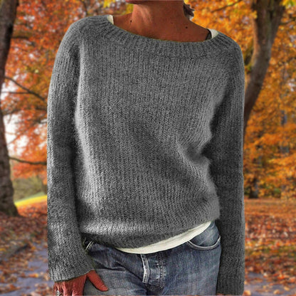 Model in the grey version of the textured knit jumper, worn over a white top and jeans with autumn trees behind. 4