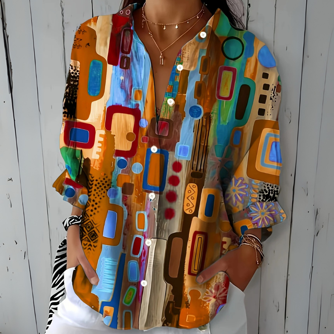 Model wearing the blouse in an orange and tan colourway with blue and red shapes, buttons undone at the neckline. 3