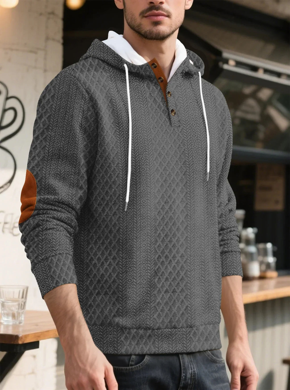 Grey textured hoodie worn by a model in three-quarter view outside a cafe, with tan elbow patch 32