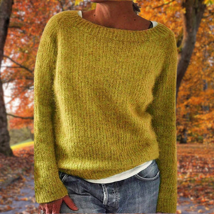 Model in a mustard-yellow knit jumper with a wide neckline, worn over a white top and jeans against autumn trees. 1