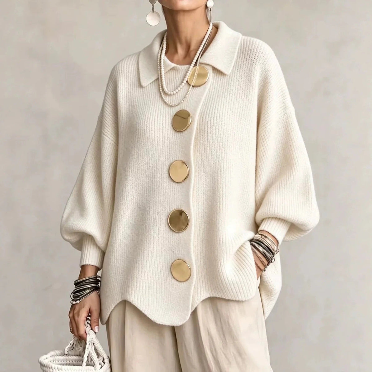 Cream ribbed cardigan on a model, with oversized gold buttons, pointed collar and wavy hem, worn with beige trousers. 4