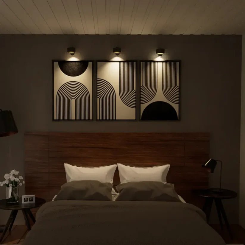 Three black wall lights above a row of three abstract framed prints, lighting a bedroom wall over a wooden headboard. 5