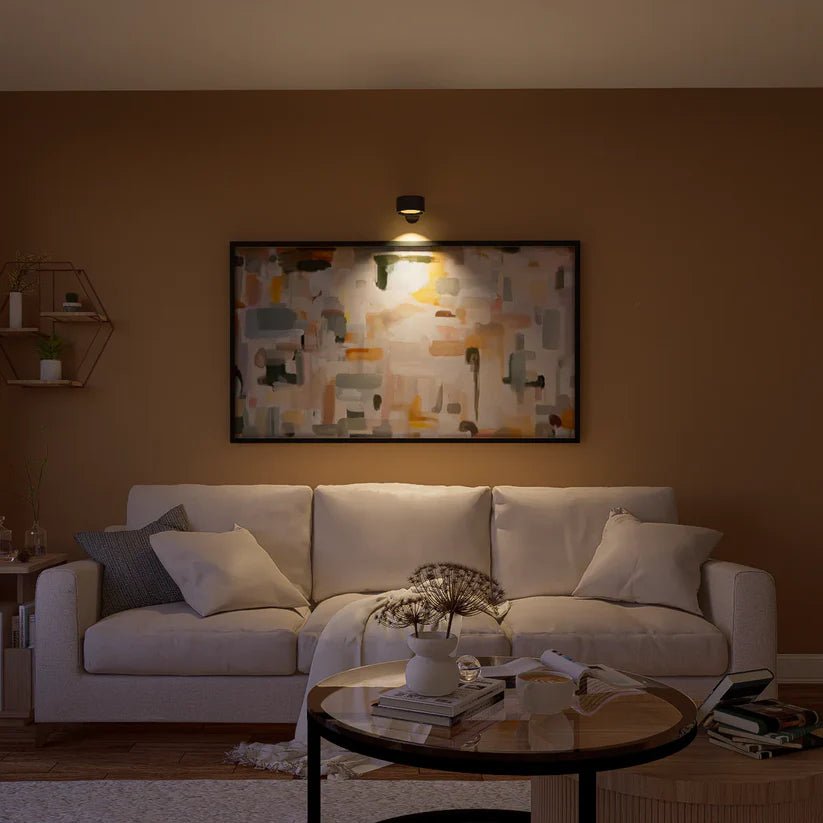 Black wall light mounted above a large abstract painting, illuminating it above a cream sofa in a living room. 8