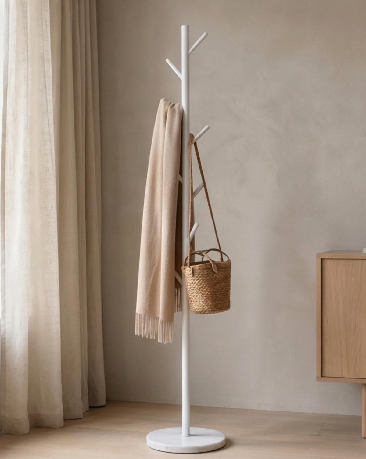 White rack with a beige fringed scarf and a woven straw basket hanging from its hooks, next to a wooden cabinet. 3