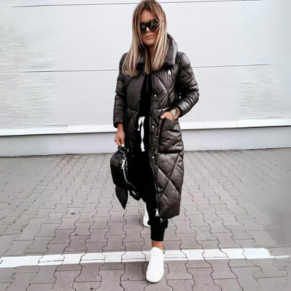 Woman with blonde hair wears the black quilted long coat zipped up, one hand in a pocket, with white trainers. 5