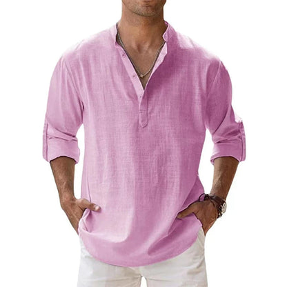 Man wearing the Henley shirt in pink, with a short button placket, rolled sleeves and hands in white trouser pockets. 3