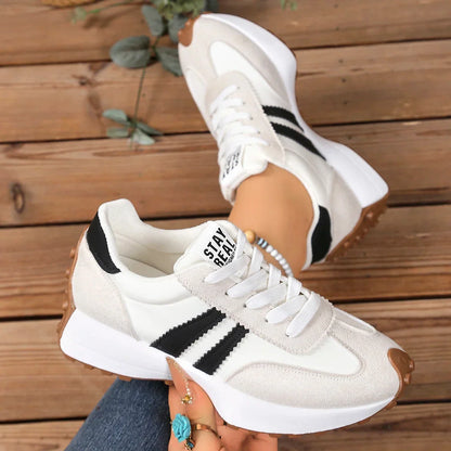White and cream trainers with black stripes, one shoe held up beside a worn pair on wooden boards 3