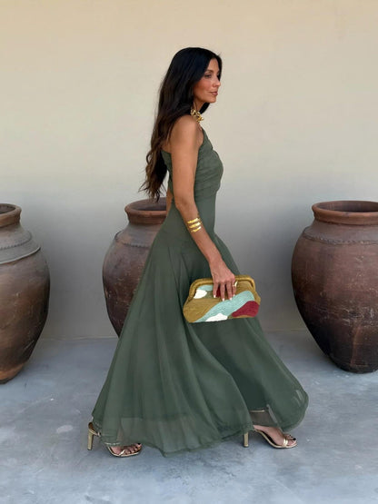 Olive green one-shoulder dress in profile, skirt swirling as the model walks past large clay pots 9