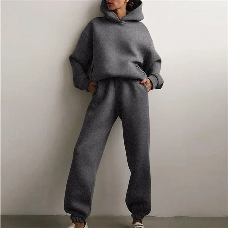 Model leaning on a wall in a dark grey hoodie and cuffed joggers, hands in pockets 3