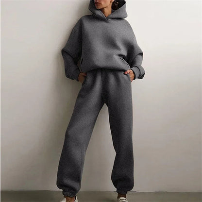 Model leaning on a wall in a dark grey hoodie and cuffed joggers, hands in pockets 3