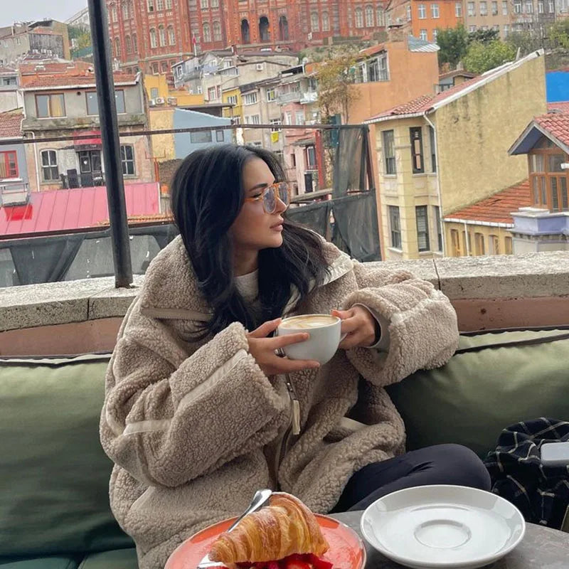 Woman in a beige fleece coat holding a coffee cup at a rooftop café table 3
