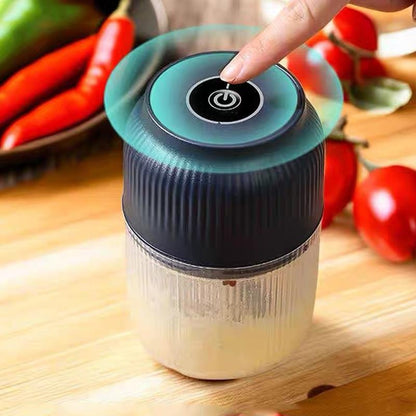Finger pressing the round power button on top of the navy ribbed lid, with chillies and tomatoes blurred behind on a wooden surface. 2