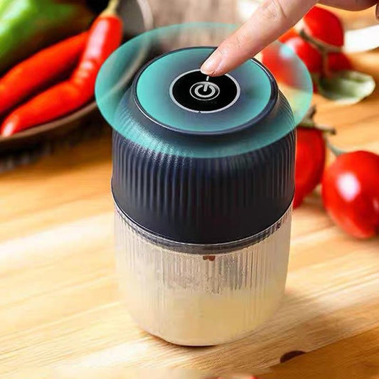 Finger pressing the round power button on top of the navy ribbed lid, with chillies and tomatoes blurred behind on a wooden surface. 2