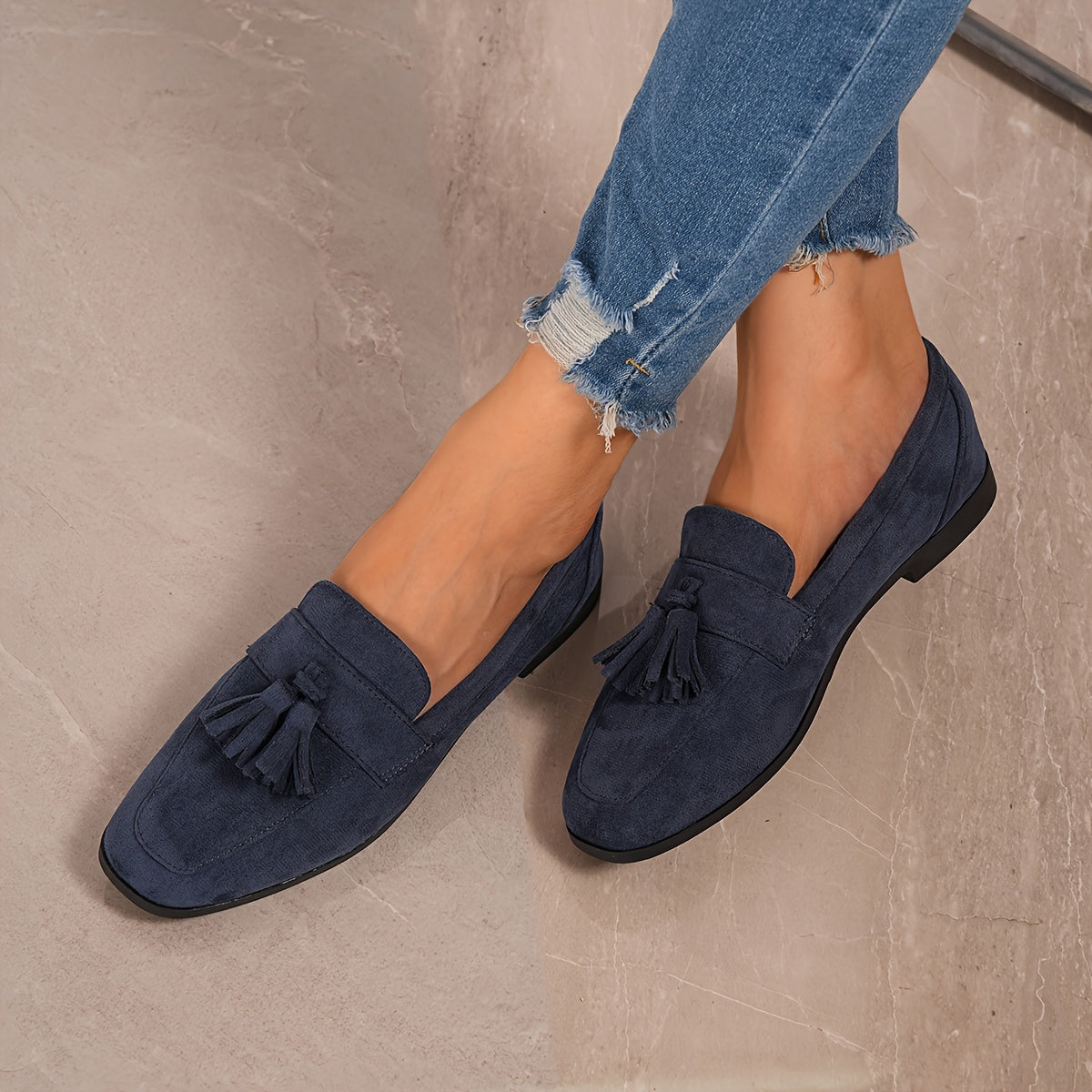 Navy tasselled loafers worn with frayed jeans, shot from above on a marbled surface 7