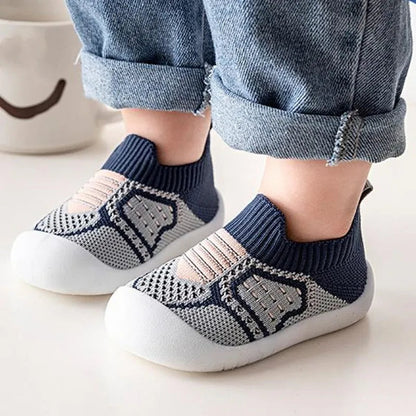 Child's feet in navy and grey knit slip-on shoes with peach stripes and white toe-capped soles, beside rolled-up denim. 8